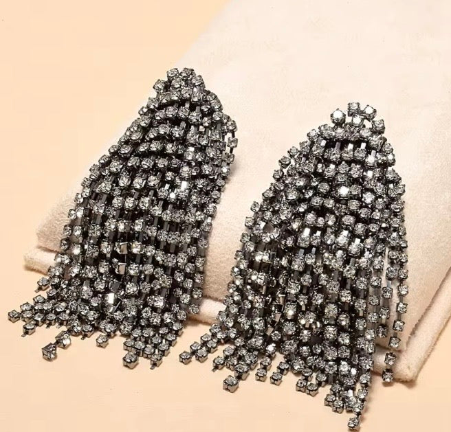 Pendientes colgantes de cristal oversize con acabados en tono metal oscuro y pedrería de tono gris.