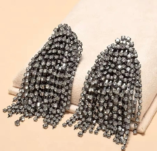 Pendientes colgantes de cristal oversize con acabados en tono metal oscuro y pedrería de tono gris.
