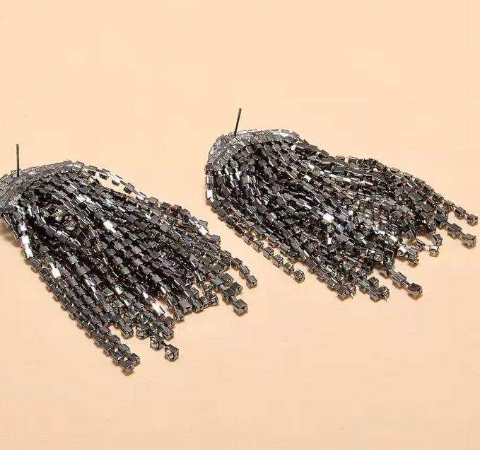 Pendientes colgantes de cristal oversize con acabados en tono metal oscuro y pedrería de tono gris.