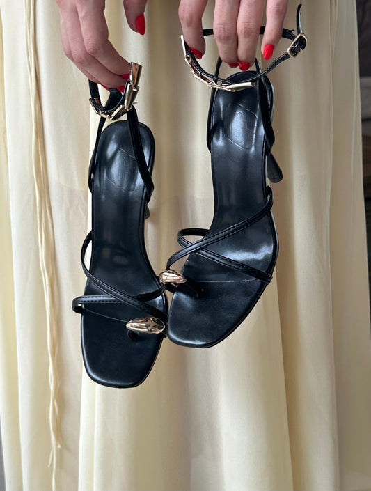 Zapatillas color negro de tira con toque dorado.