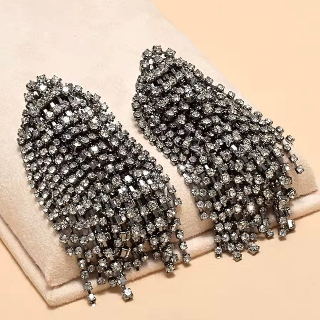 Pendientes colgantes de cristal oversize con acabados en tono metal oscuro y pedrería de tono gris.